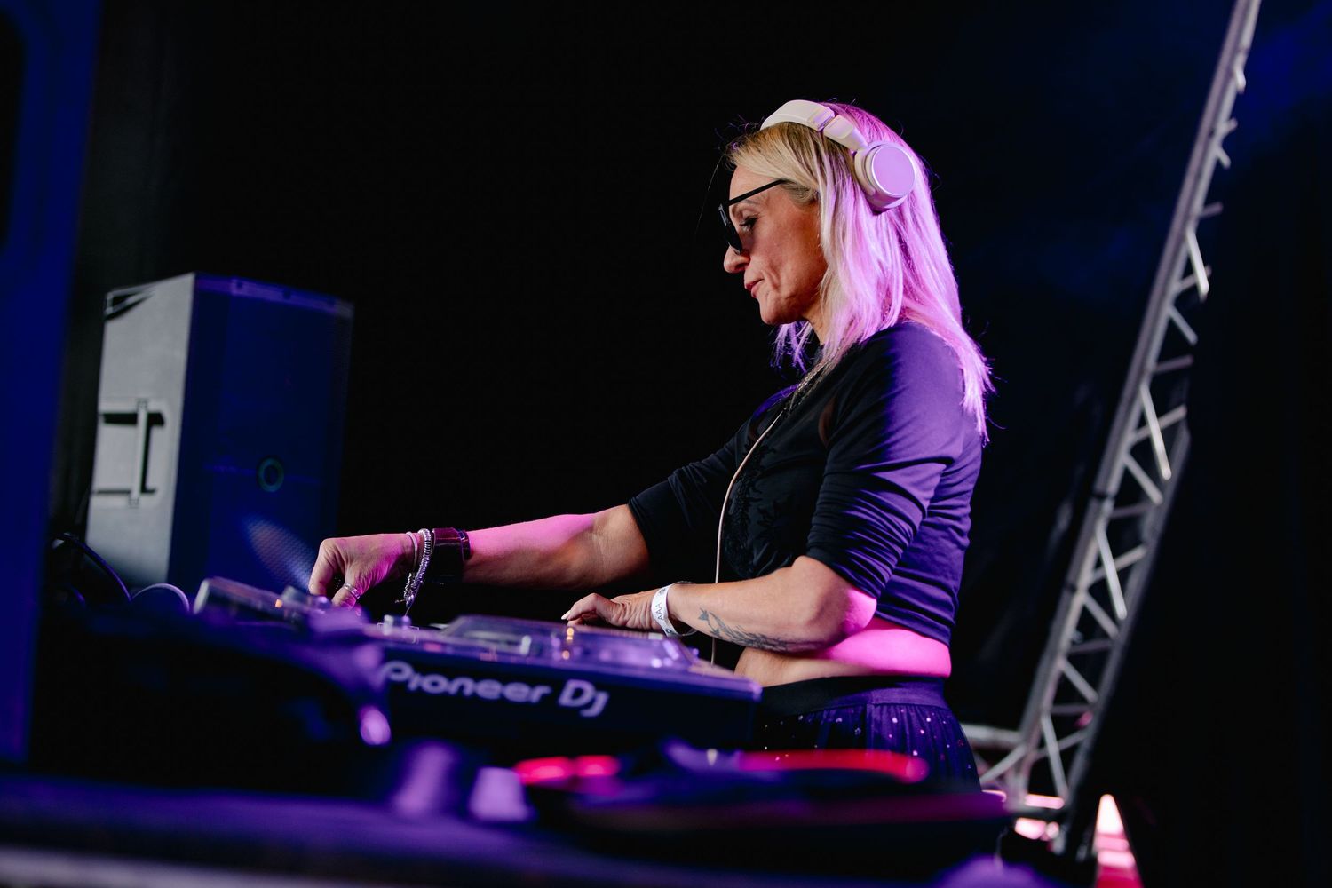 DJ working the controls at a professional mixing station under purple stage lights.