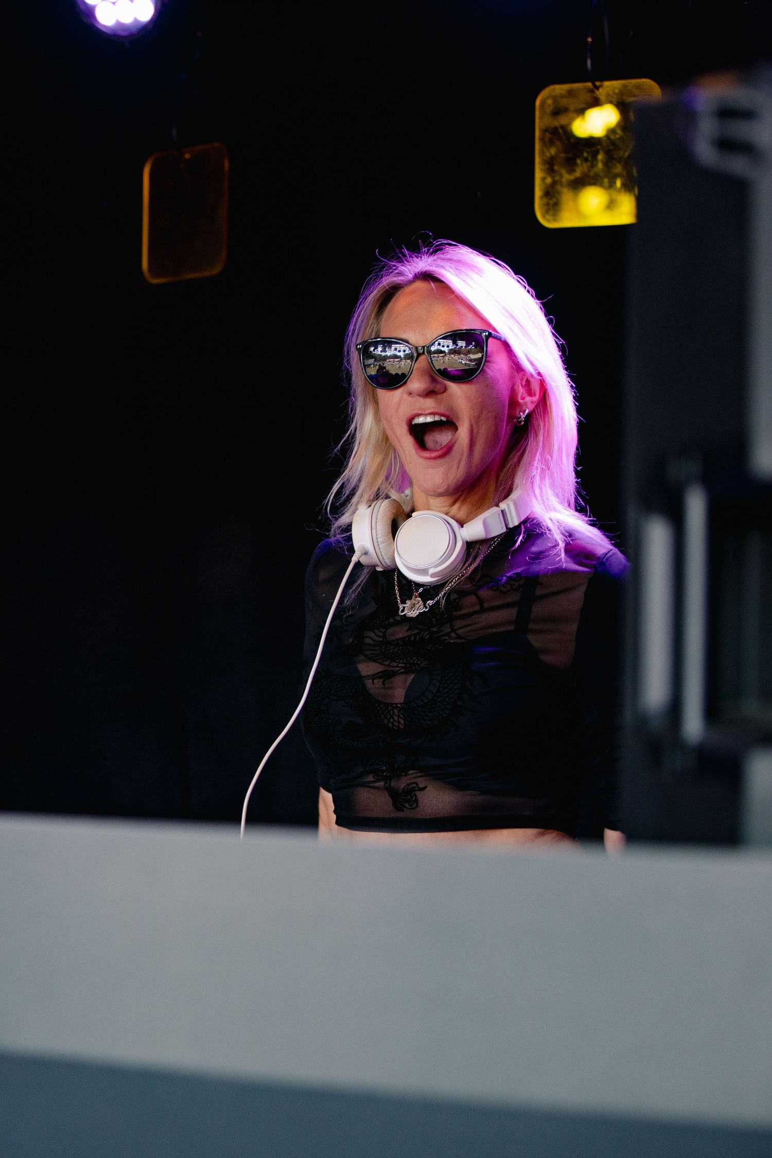 Performer in black outfit enthusiastically DJing under colorful stage lighting.