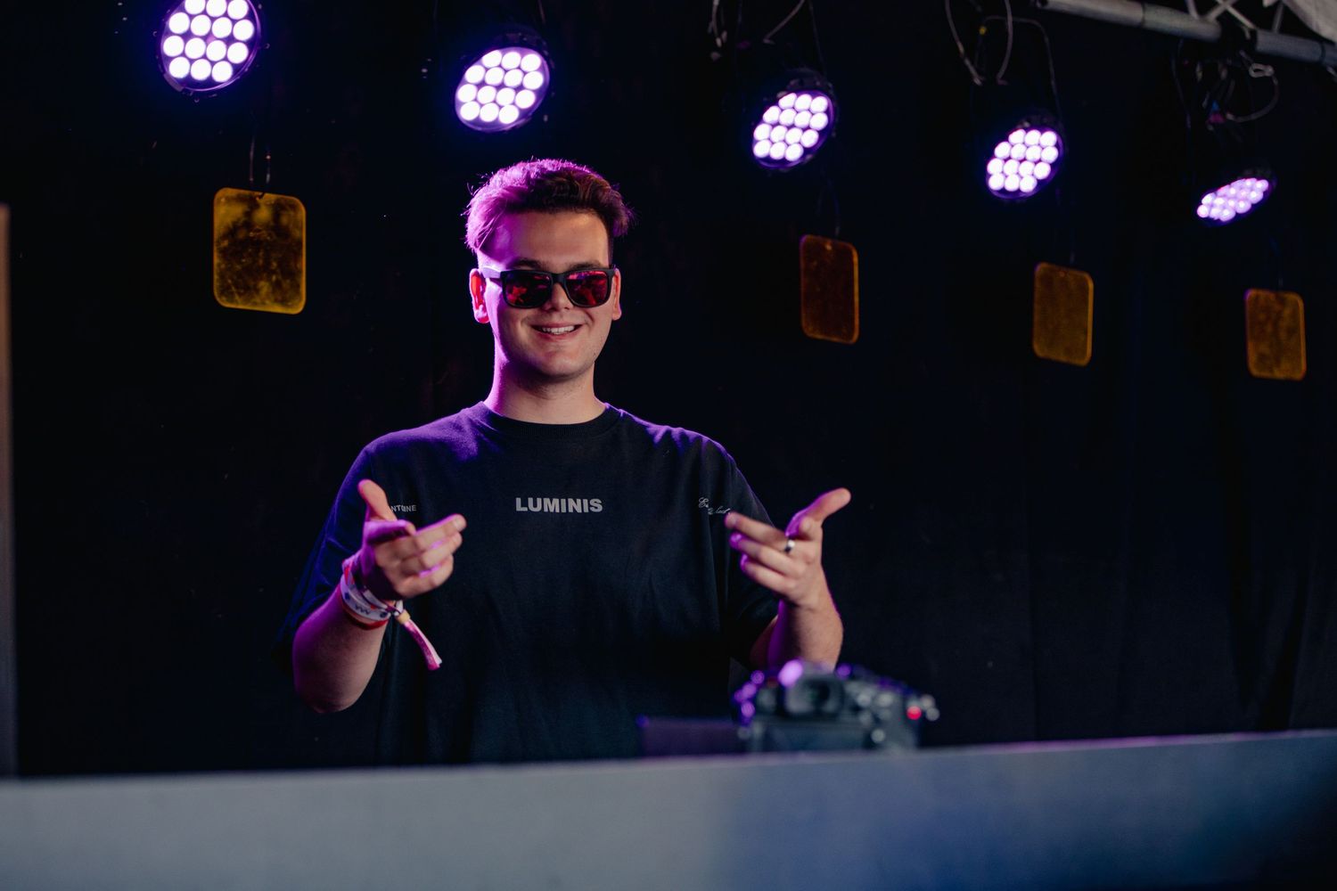 DJ performing at a nightclub with purple stage lighting and professional equipment setup.