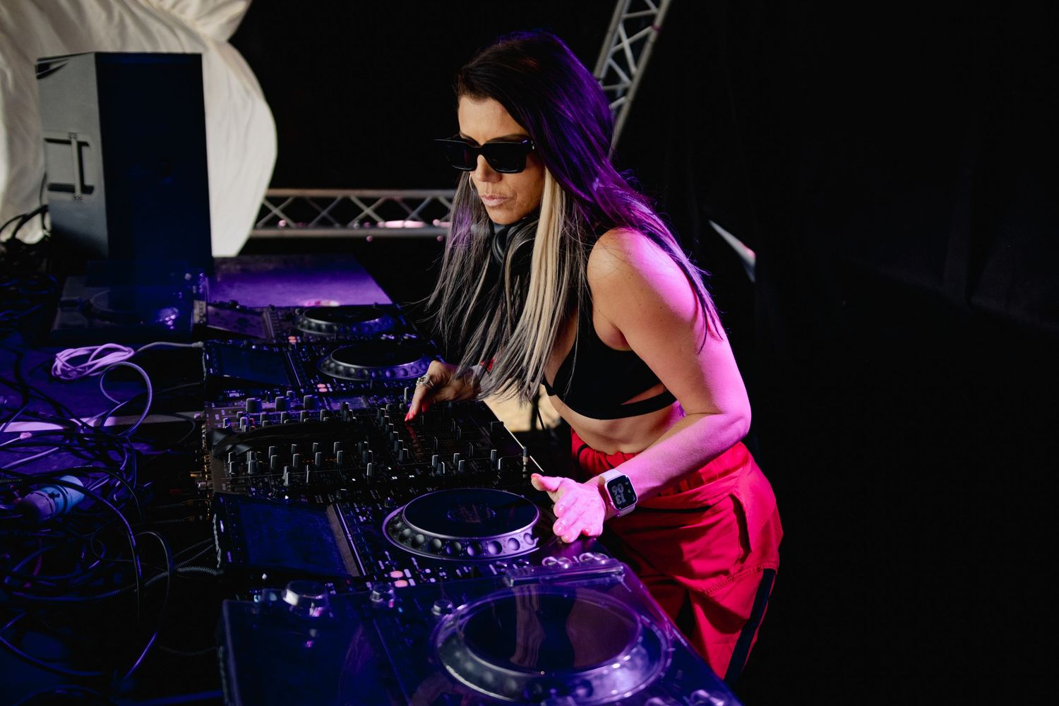 DJ working the turntables and mixer controls in a dark venue with stage lighting.