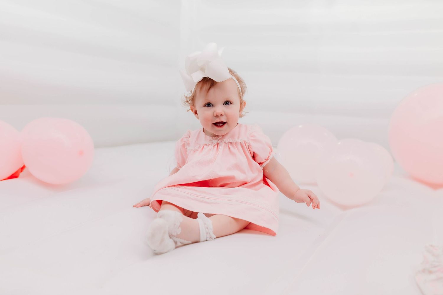 Baby photography scene with pink balloons and soft white backdrop.