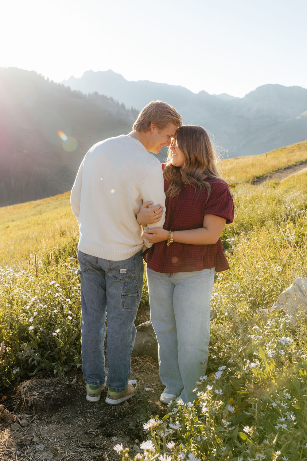 Couple touching foreheads tenderly in a wildflower alpine meadow at sunset.