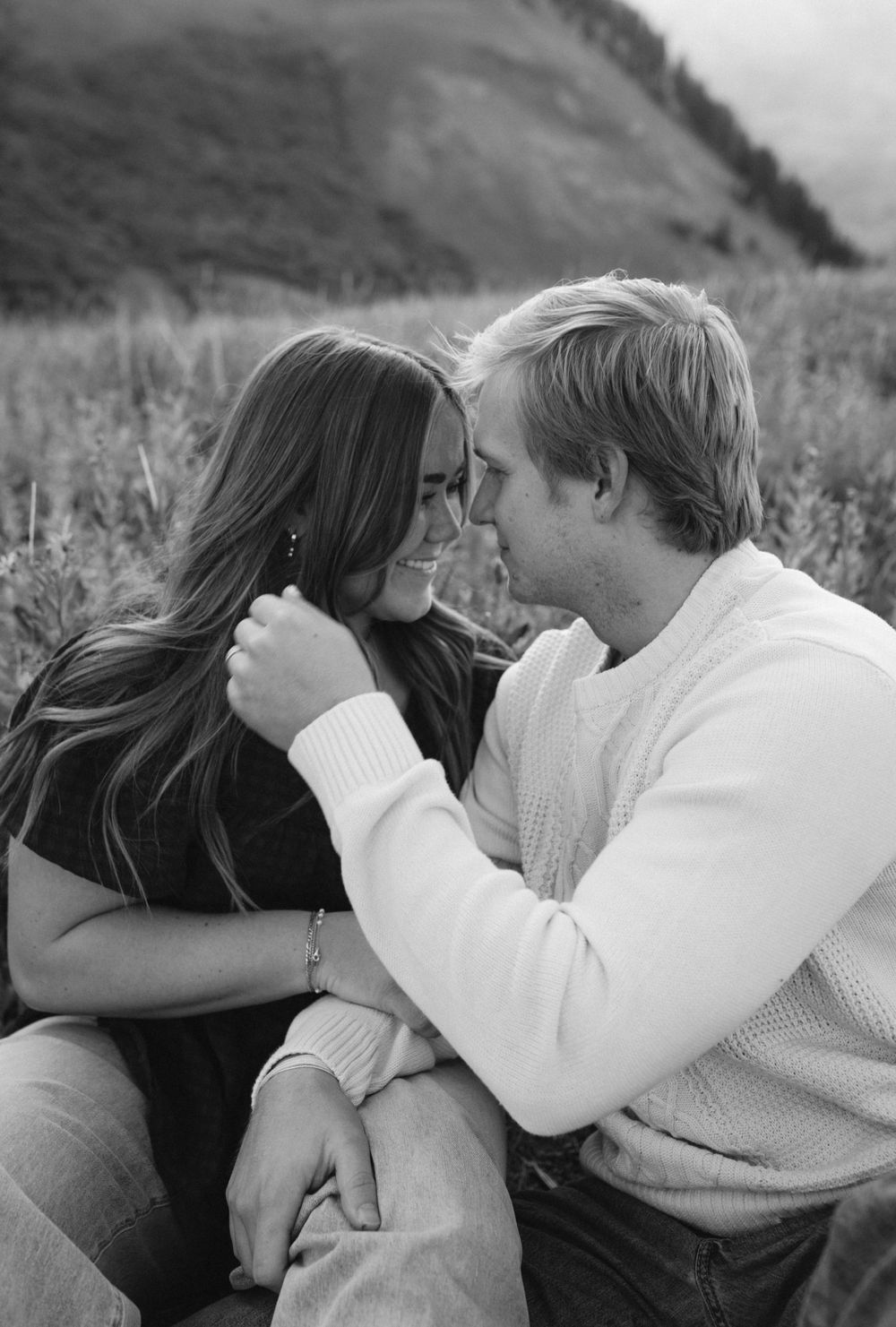 Black and white photo of a couple sharing a tender moment in a mountain meadow.