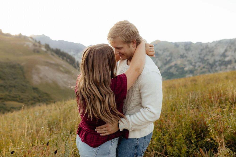 A couple shares a romantic embrace in a mountain meadow at sunset.