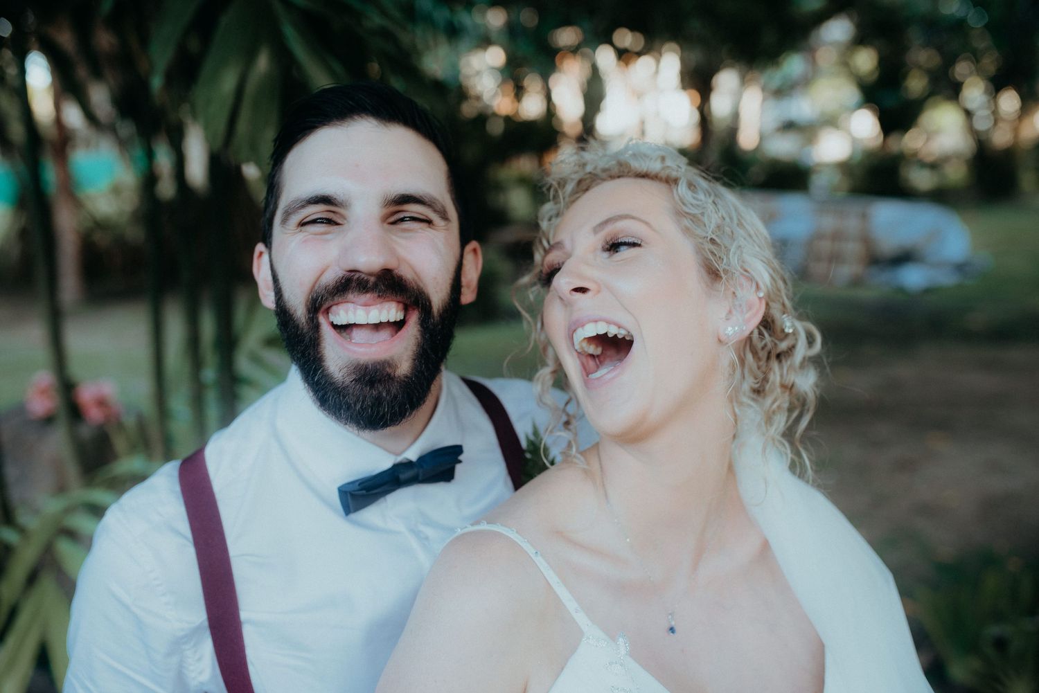 Joyful wedding couple laughing outdoors in casual attire.