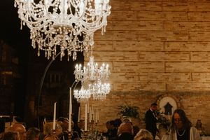 Elegant crystal chandeliers hang from a rustic brick ceiling at a wedding reception.