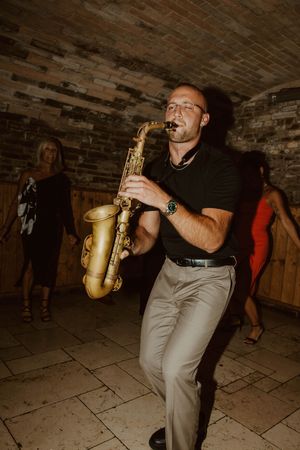 Musician plays saxophone in a rustic brick-walled venue.