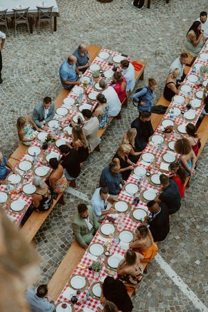 Overhead view of outdoor dinner party with red checkered tablecloths and place settings.