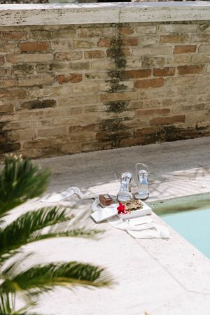 Sandals and papers laid out by a pool with a brick wall and palm fronds.