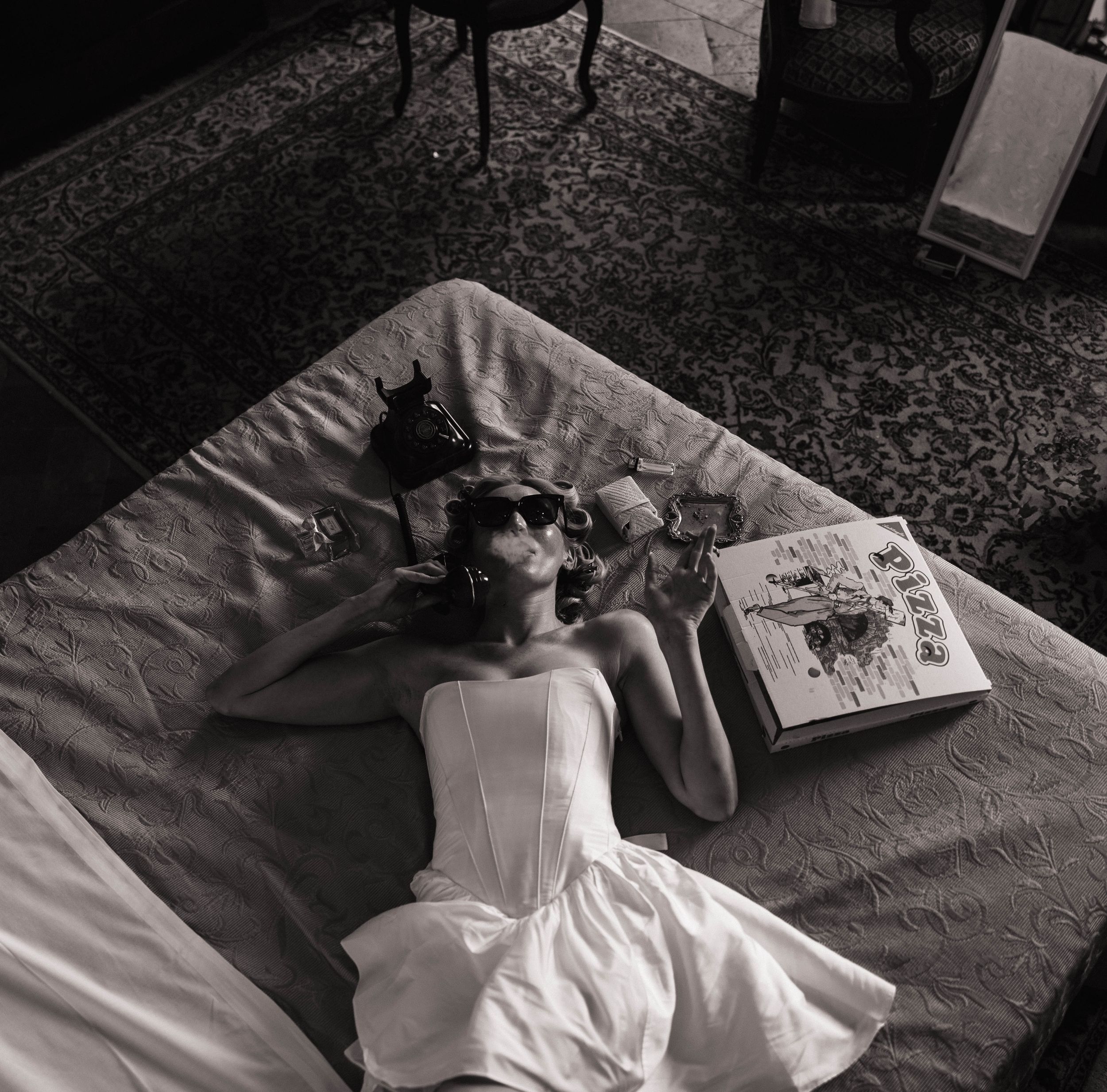 Artistic black and white photo of person in white dress laying on textured surface.