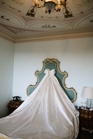 Wedding dress displayed against turquoise headboard under ornate ceiling with chandelier.