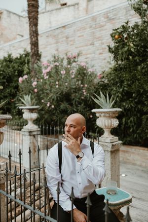 Person in white shirt and suspenders standing by decorative garden urns.