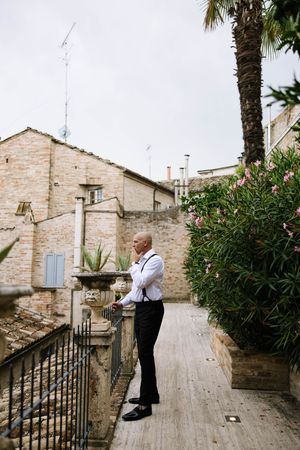 Person in formal attire standing on stone path beside palm trees and garden.