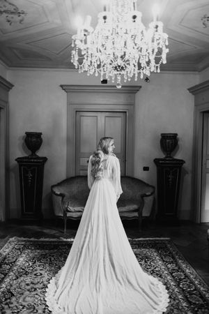 Bride in flowing white gown and veil poses in an elegant room with crystal chandeliers.