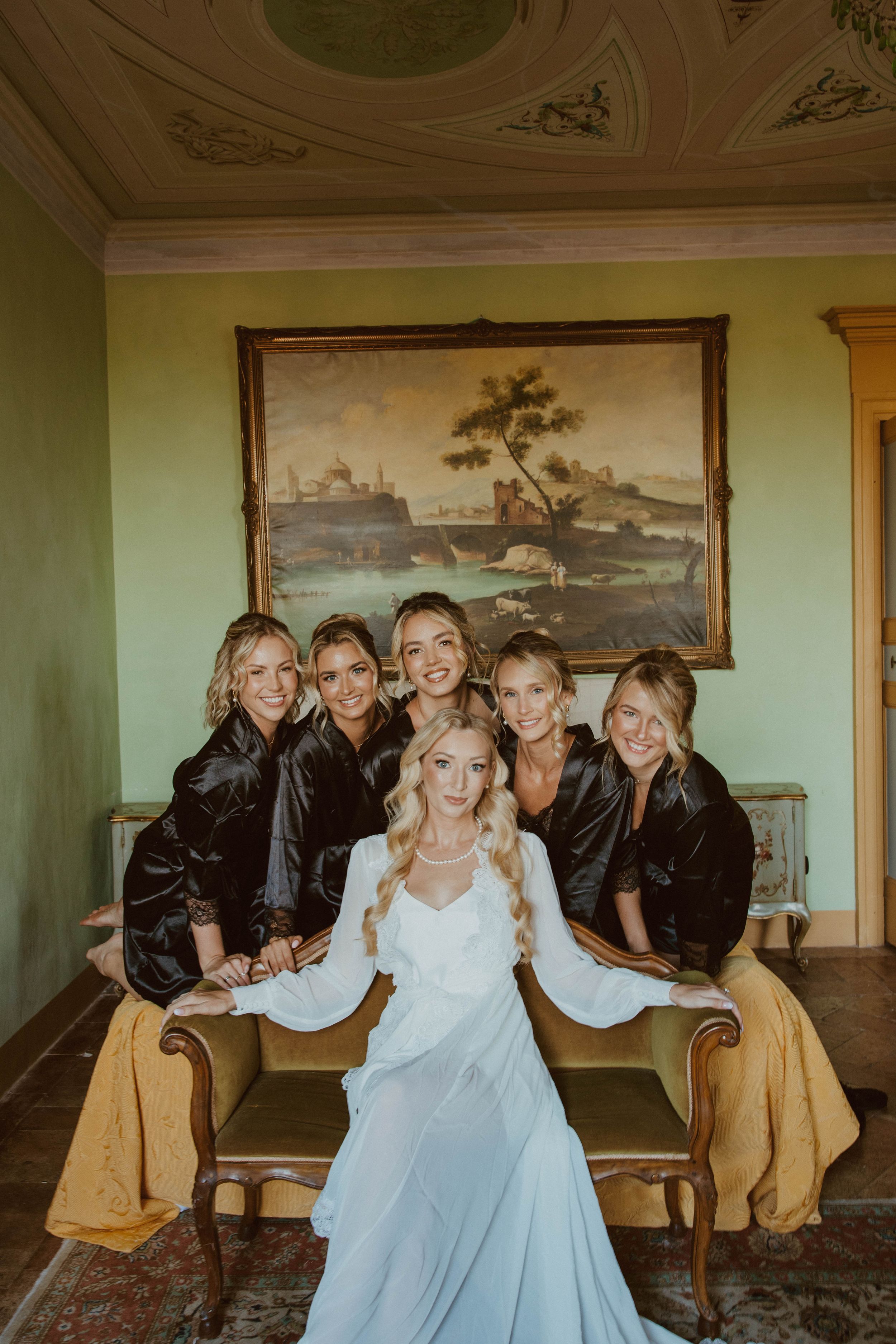 A group in formal attire poses together on an antique sofa in a room with vintage decor.