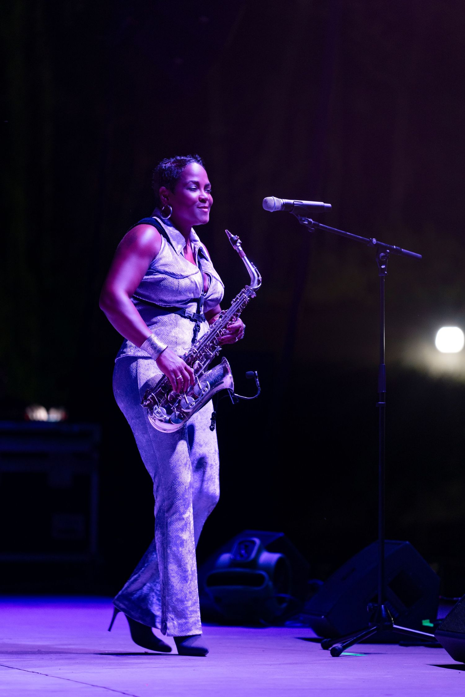 A performer in white plays saxophone on a dimly lit stage illuminated by purple lighting during a musical performance.