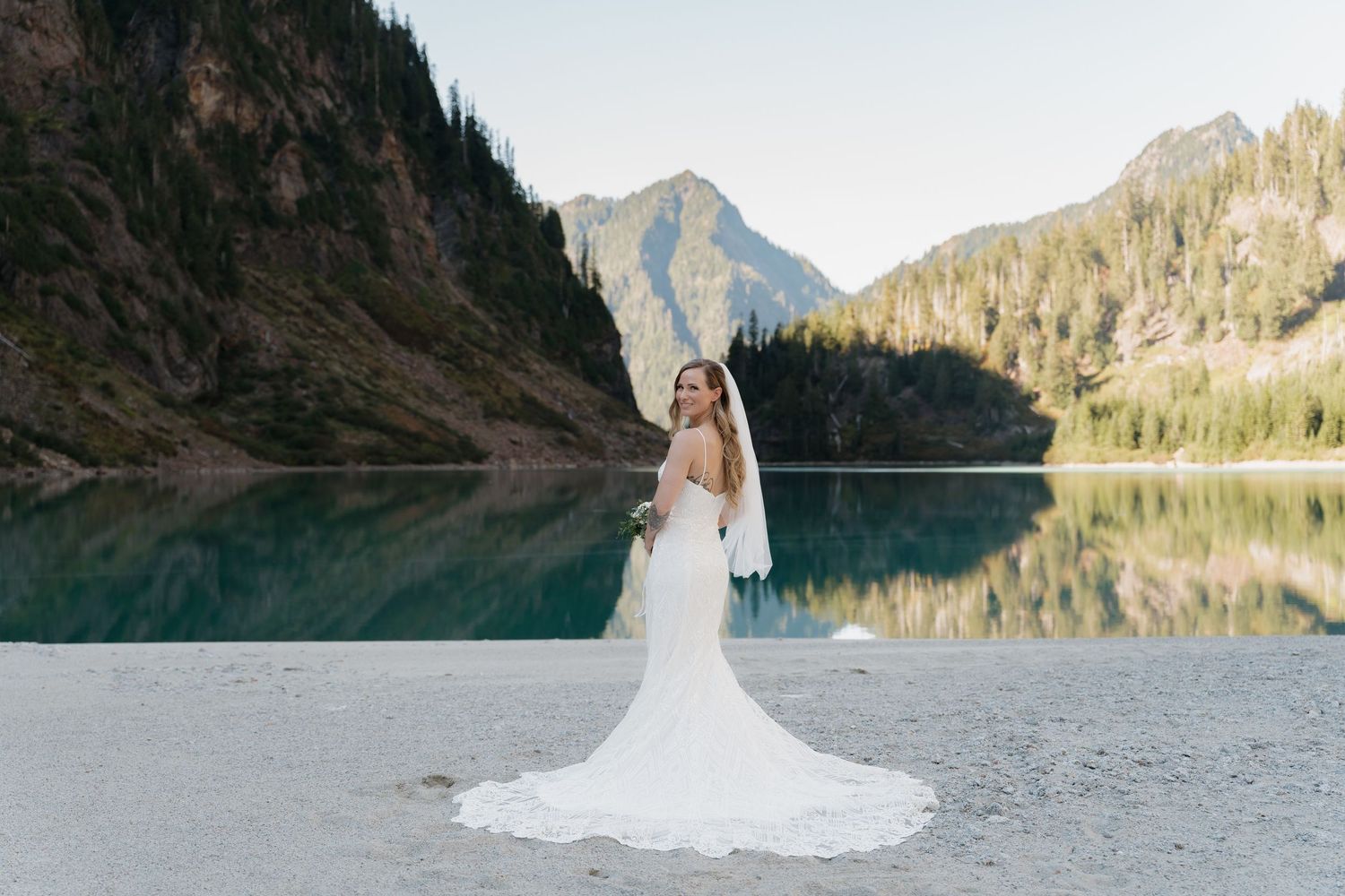 A scenic mountain lake provides a stunning backdrop for a wedding photoshoot with a white lace gown.