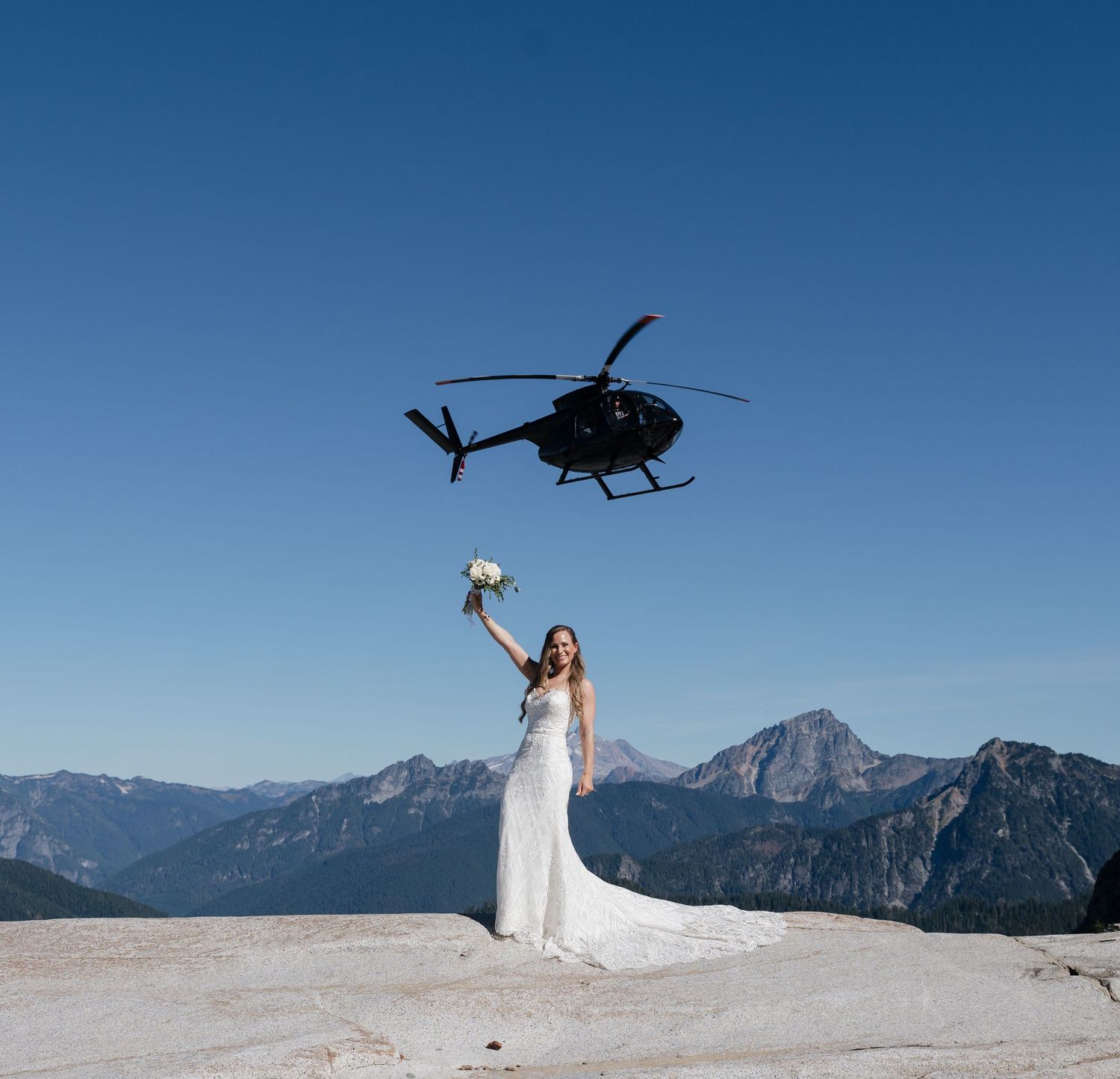 A dramatic wedding photo with a helicopter hovering above against mountain peaks.