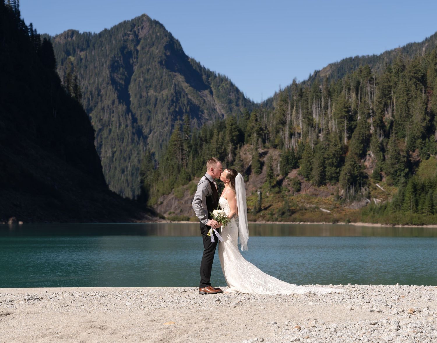 A romantic lakeside wedding moment with mountains and forest in the background.