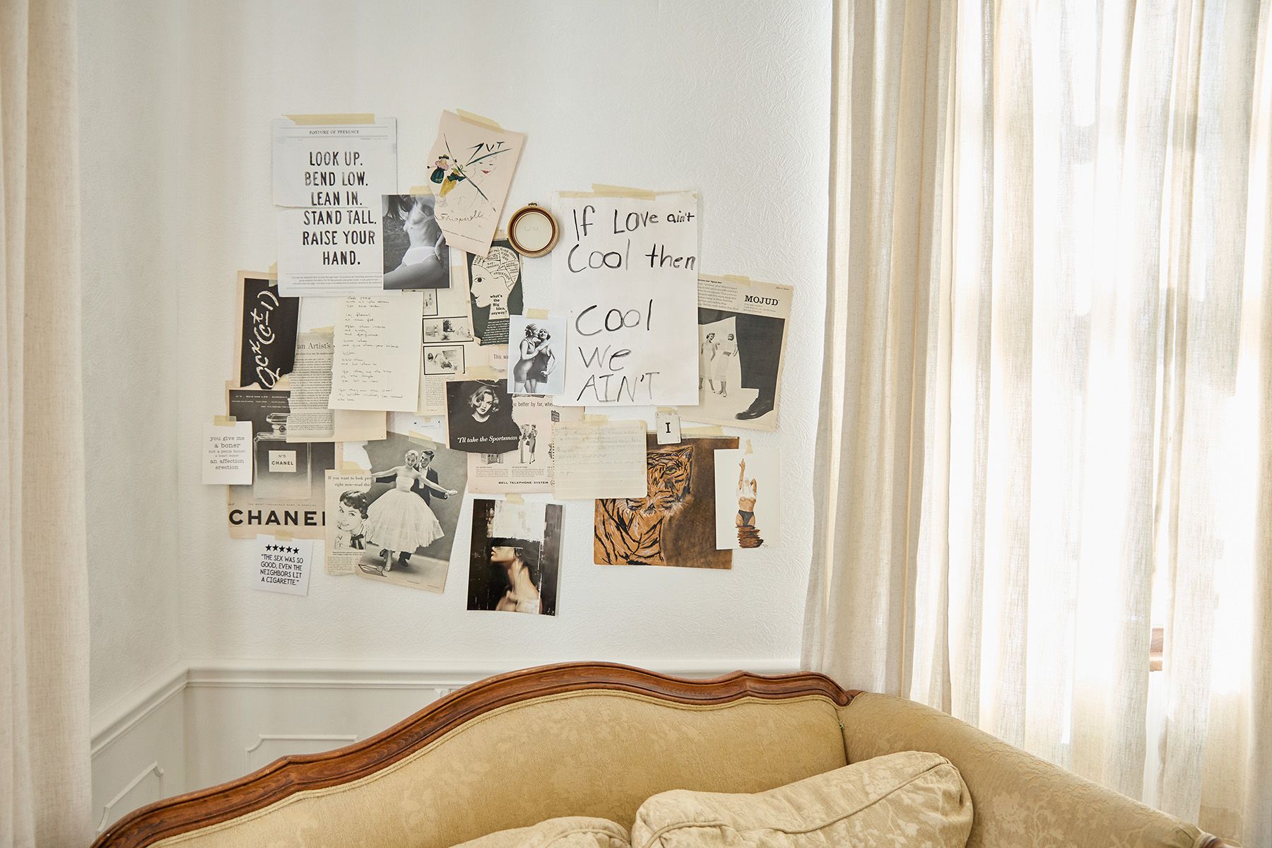 Artistic mood board with photos and notes displayed above vintage couch near window.
