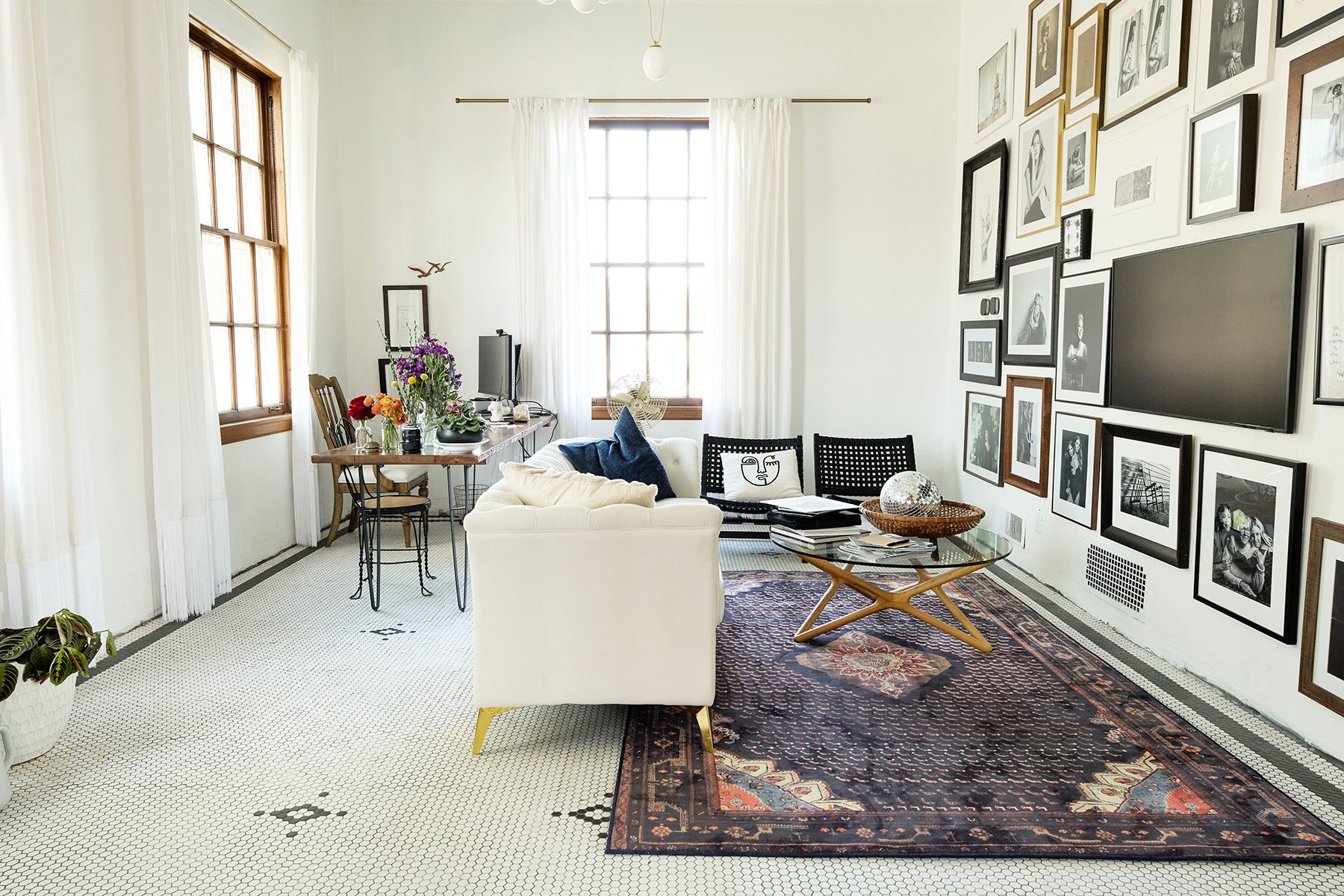 Bright studio space with white sofa, colorful rug, and wall of framed artwork.