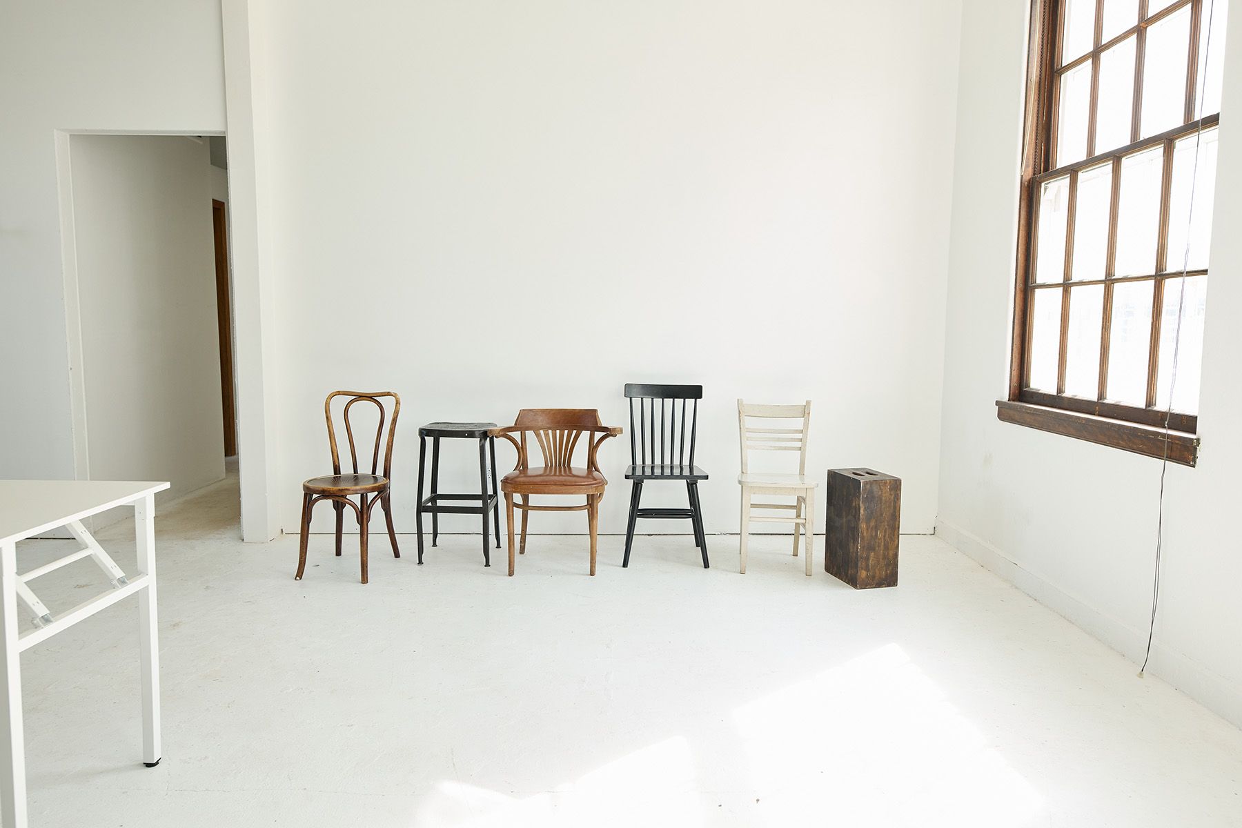 Minimalist white room with assorted wooden chairs arranged against wall.
