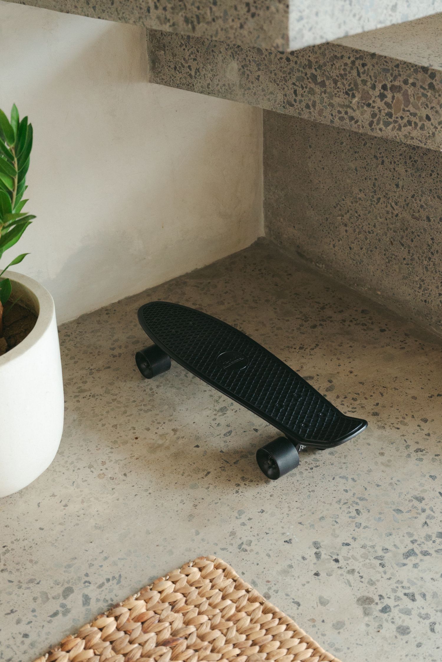 A black gun magazine lies on a speckled gray concrete floor next to a white ceramic vase with green foliage.