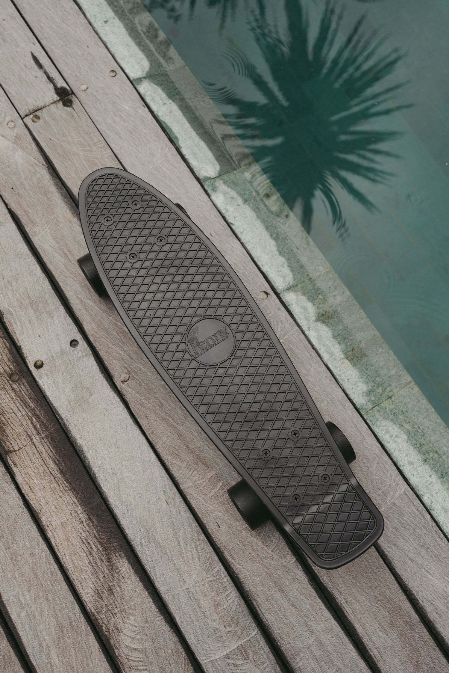 Black skateboard deck with geometric pattern grip tape rests on weathered wooden deck boards.