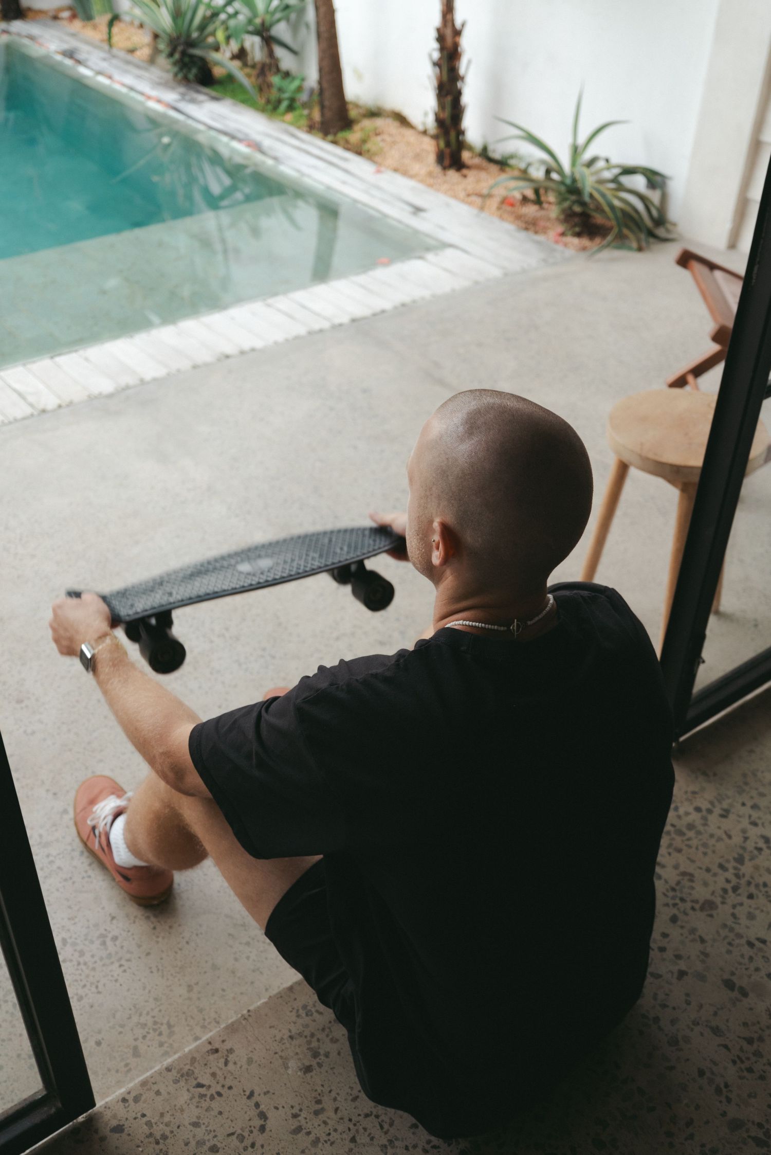 Person in black shirt relaxing on patio near swimming pool with tropical landscaping in background.