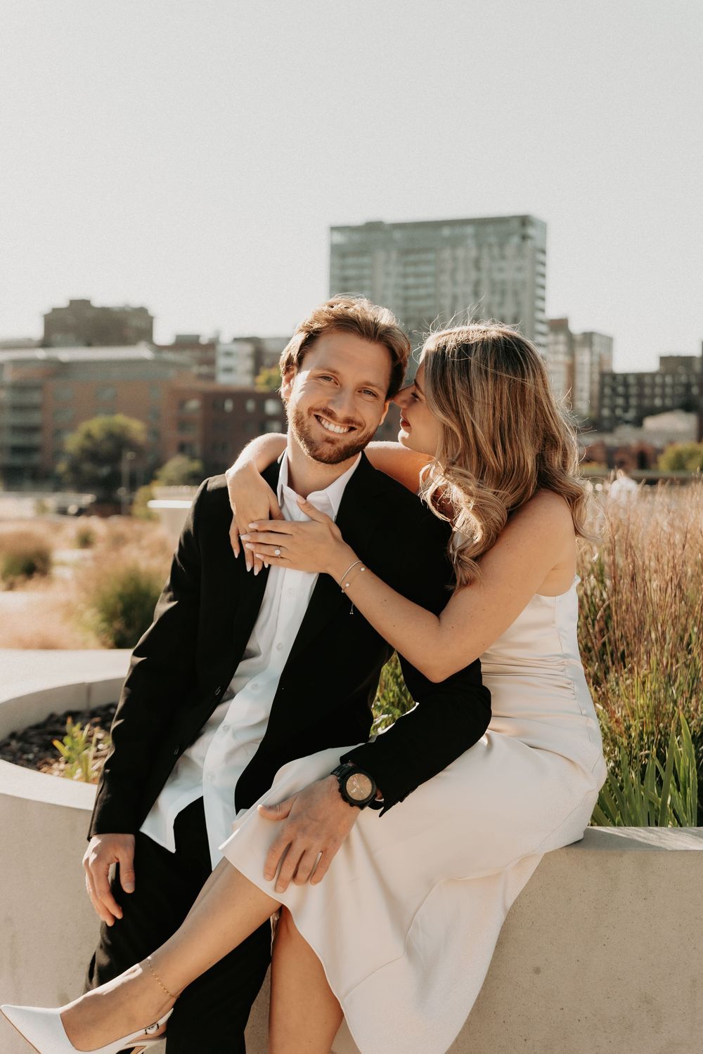 Couple shares playful and candid moments together on a rooftop terrace with urban buildings in background.