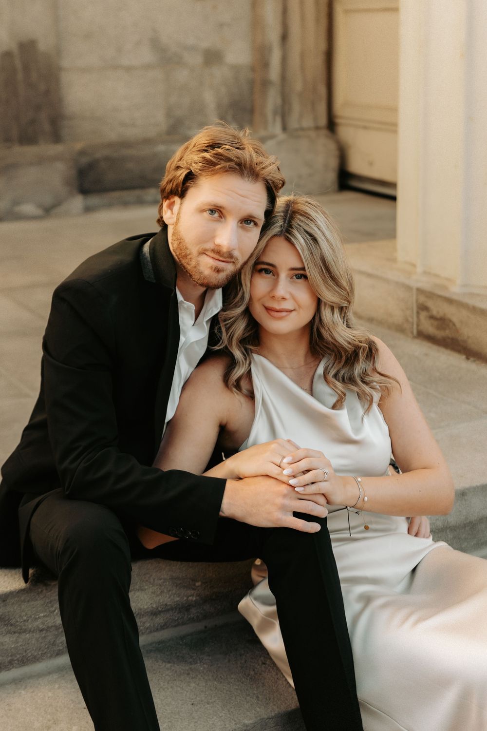 Romantic couple in formal attire poses intimately together in an outdoor architectural setting with stone columns.