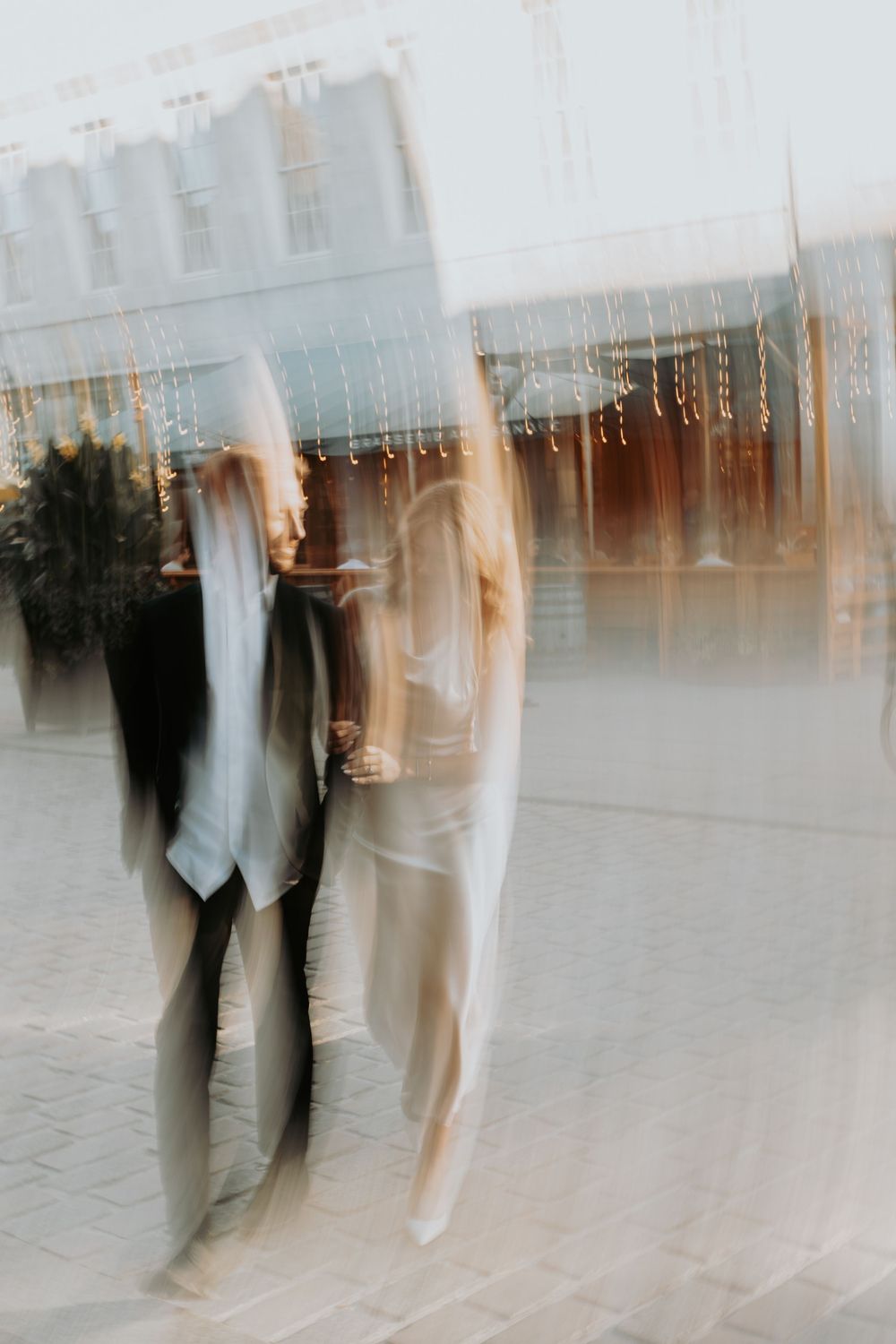 Artistic motion blur photograph of two people standing together under hanging string lights creating a dreamy atmosphere.