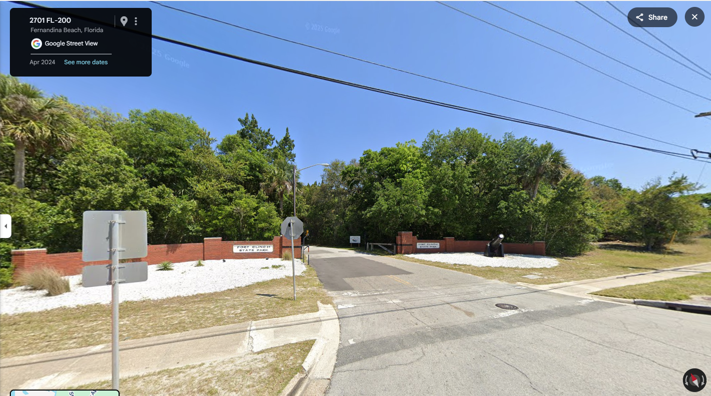 Google Street View of a suburban Florida intersection with red brick wall and palm trees.