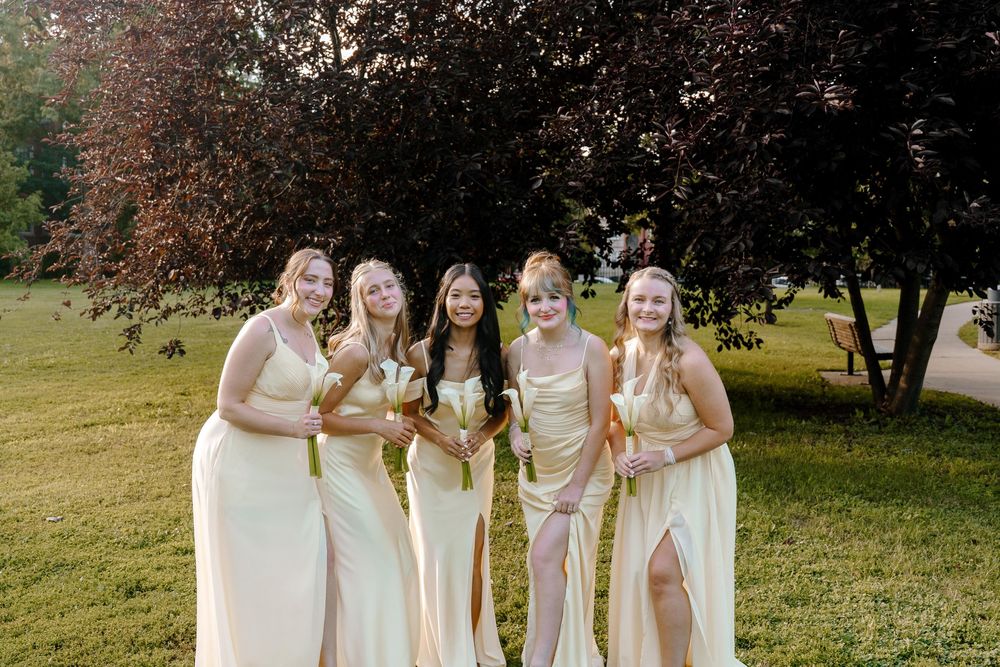 Wedding party in coordinated cream-colored dresses posing together on a sloping lawn.