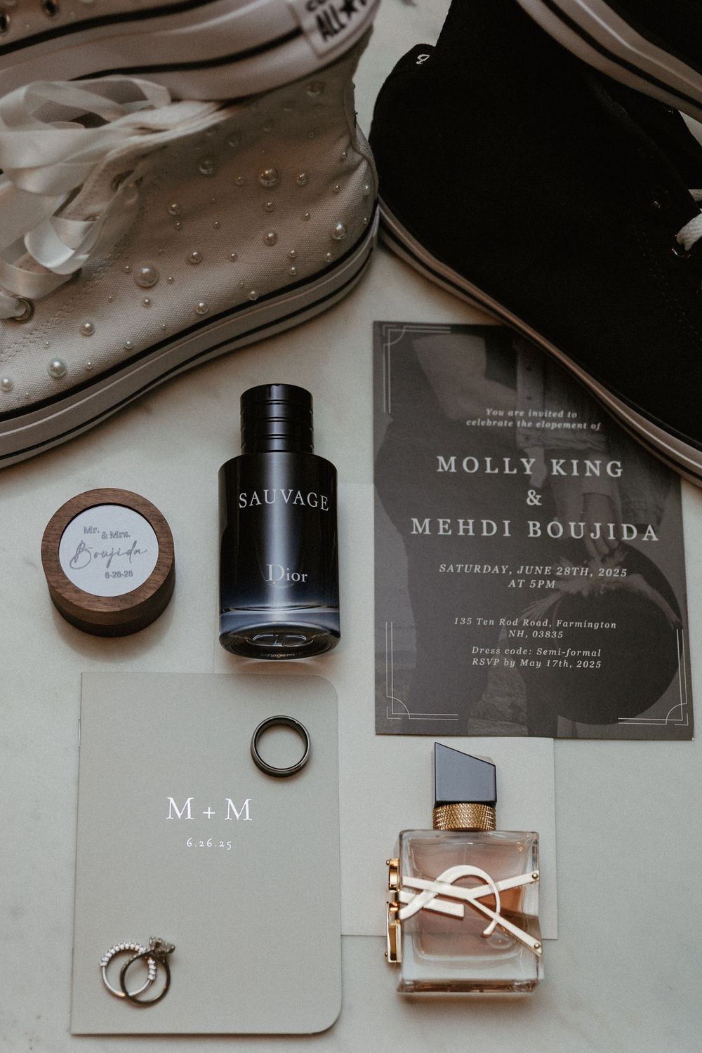 Modern wedding invitation cards and perfume bottles styled with rings in monochromatic theme.