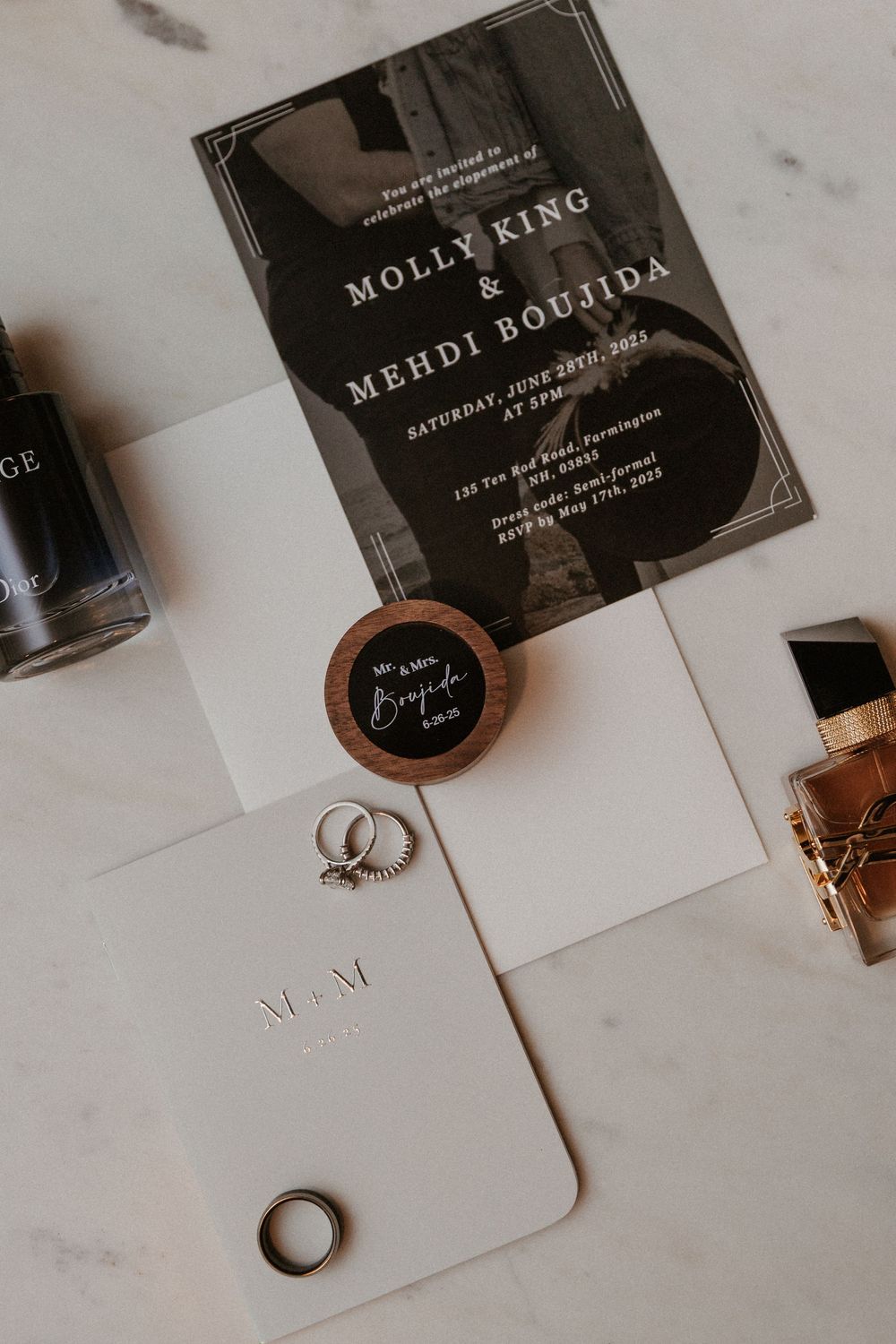 Wedding stationery and rings arranged on white marble surface with elegant typography.
