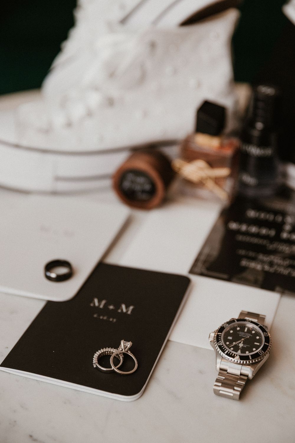 Wedding accessories including rings and watch arranged on white surface with black cards.