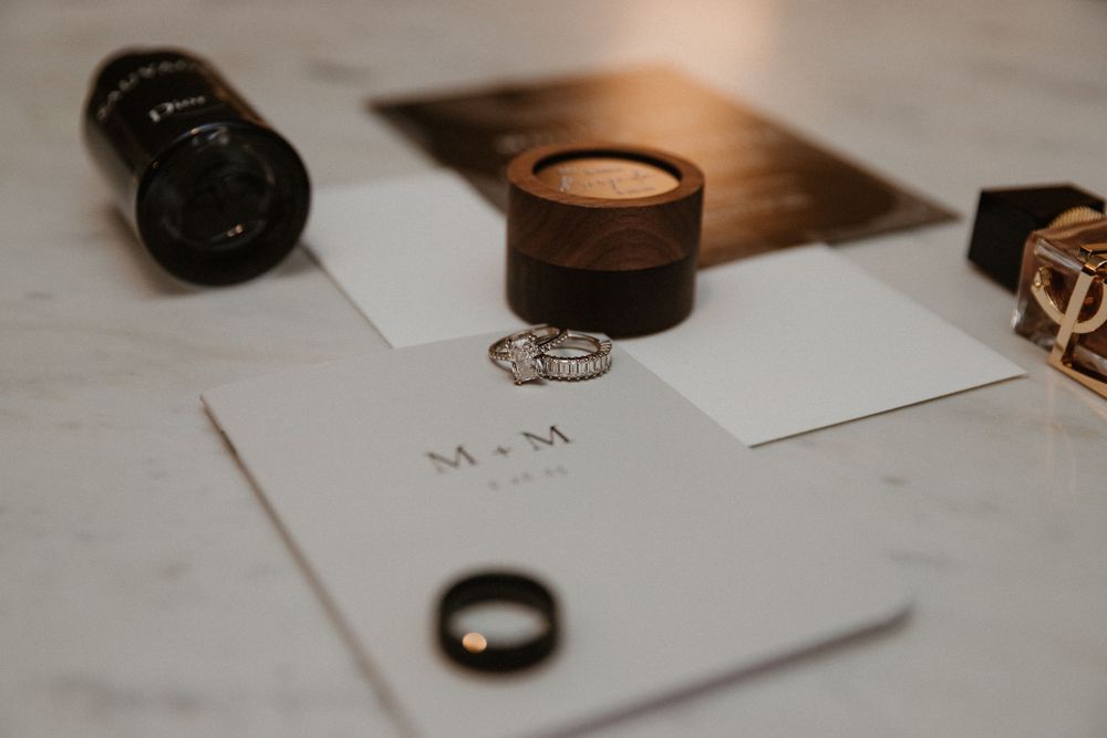 Minimalist wedding invitation details with rings on white marble background.