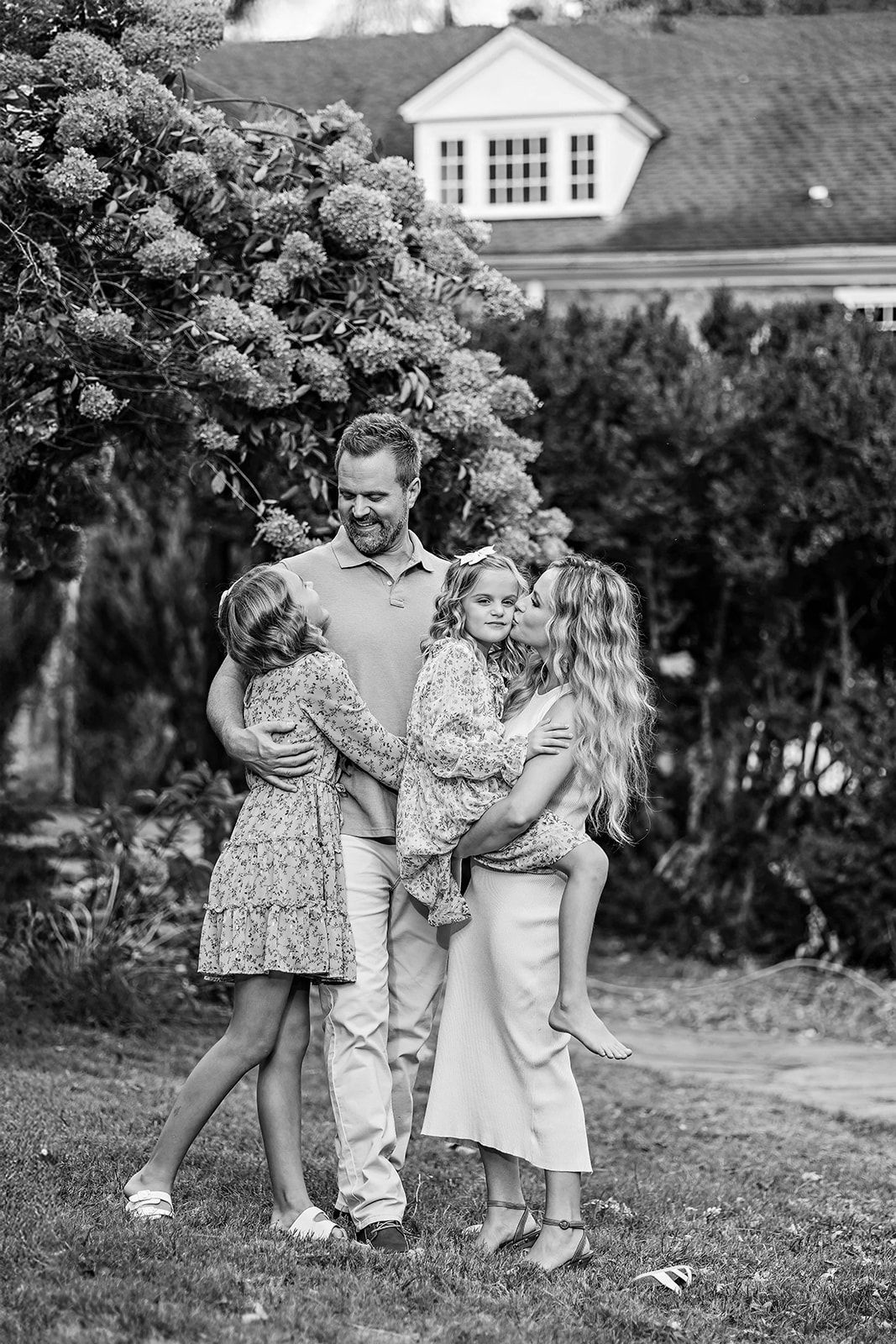 A black and white candid photo of a family of 4, embracing outdoors near Mechanicsburg PA in Cumberland County.