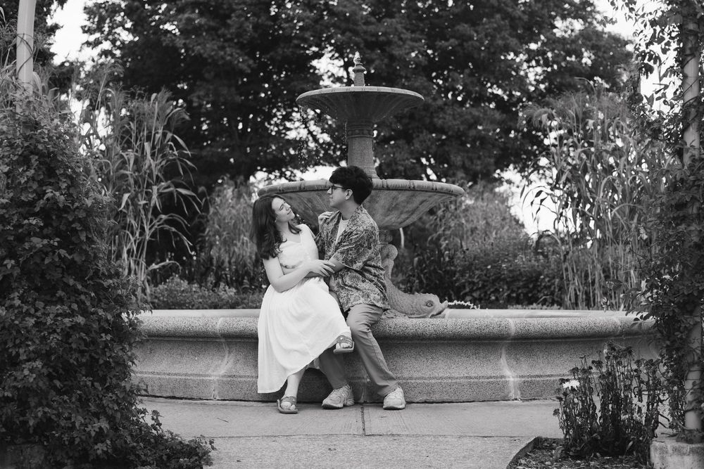 A couple relaxes on a picnic blanket in a tranquil garden setting with dappled sunlight.