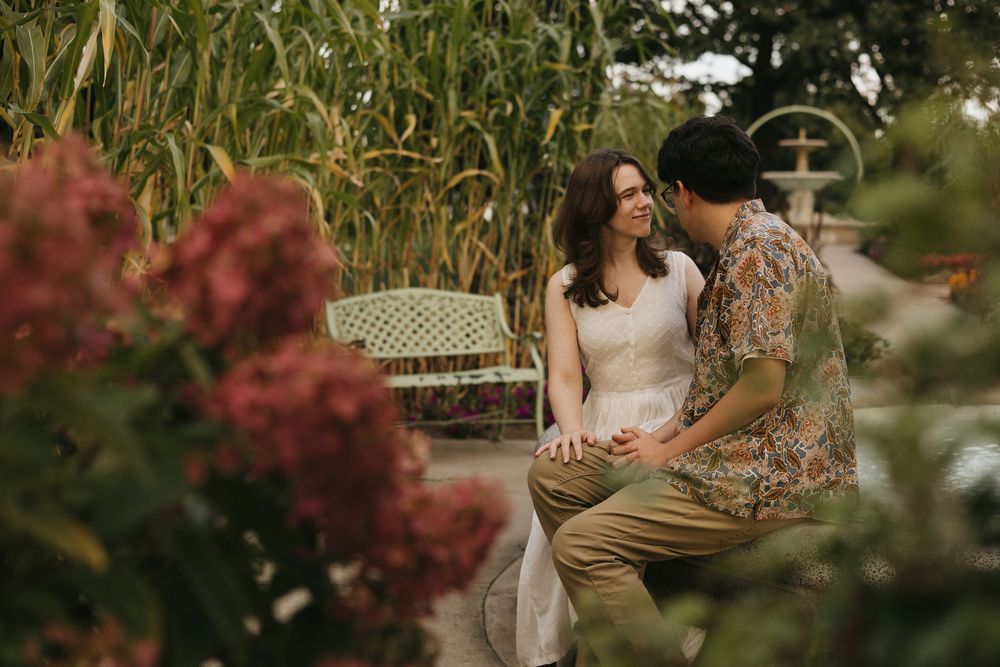 A romantic garden picnic scene with autumn foliage and flowering plants in the background.