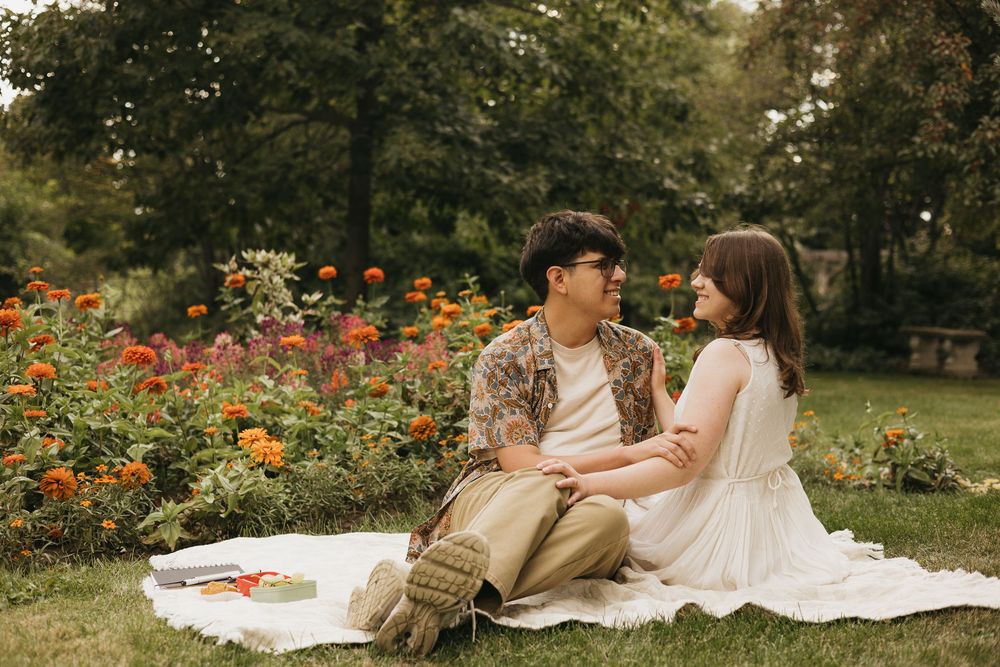 A couple enjoys a romantic picnic in a lush garden setting with blooming flowers and greenery.