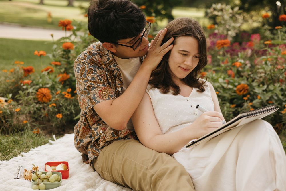 A couple shares an intimate moment while having a picnic on a blanket surrounded by roses.