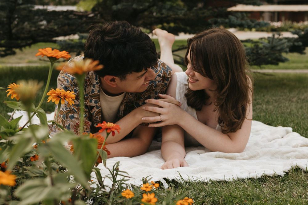 A couple lying on a white blanket in a garden with orange flowers blooming around them.