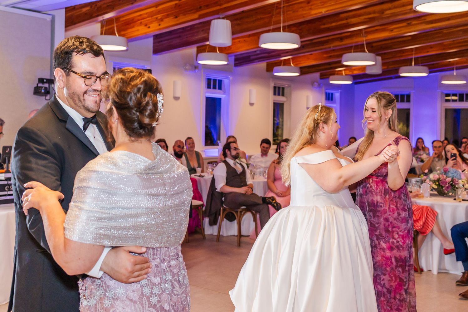 Couples dance together at an elegant wedding reception with purple uplighting and wooden beam ceilings.