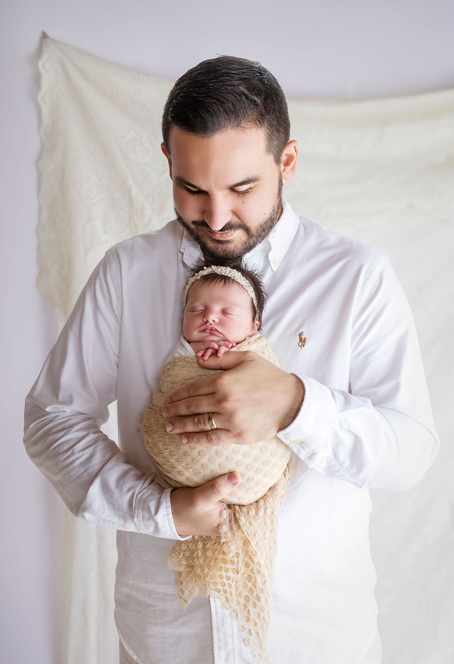 papa vestido de blanco posa con su bebe en las manos bebe es recien nacida