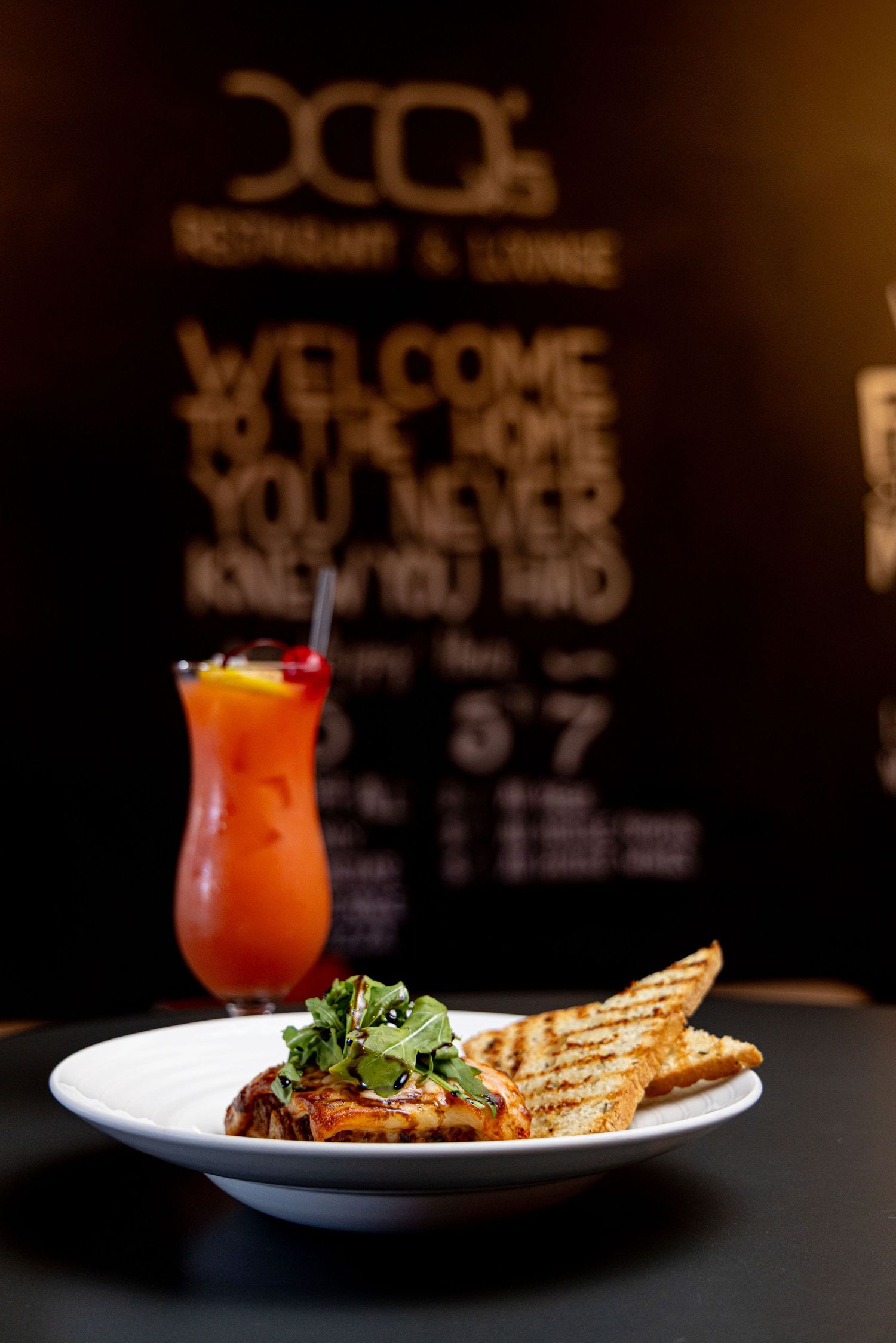 Artfully plated dishes and cocktails on dark tables with chalkboard menu backgrounds in a restaurant setting.