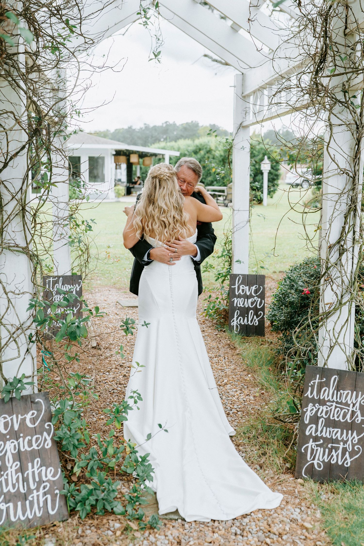 A romantic wedding moment captured under a floral arch with rustic chalkboard signs displaying love quotes.