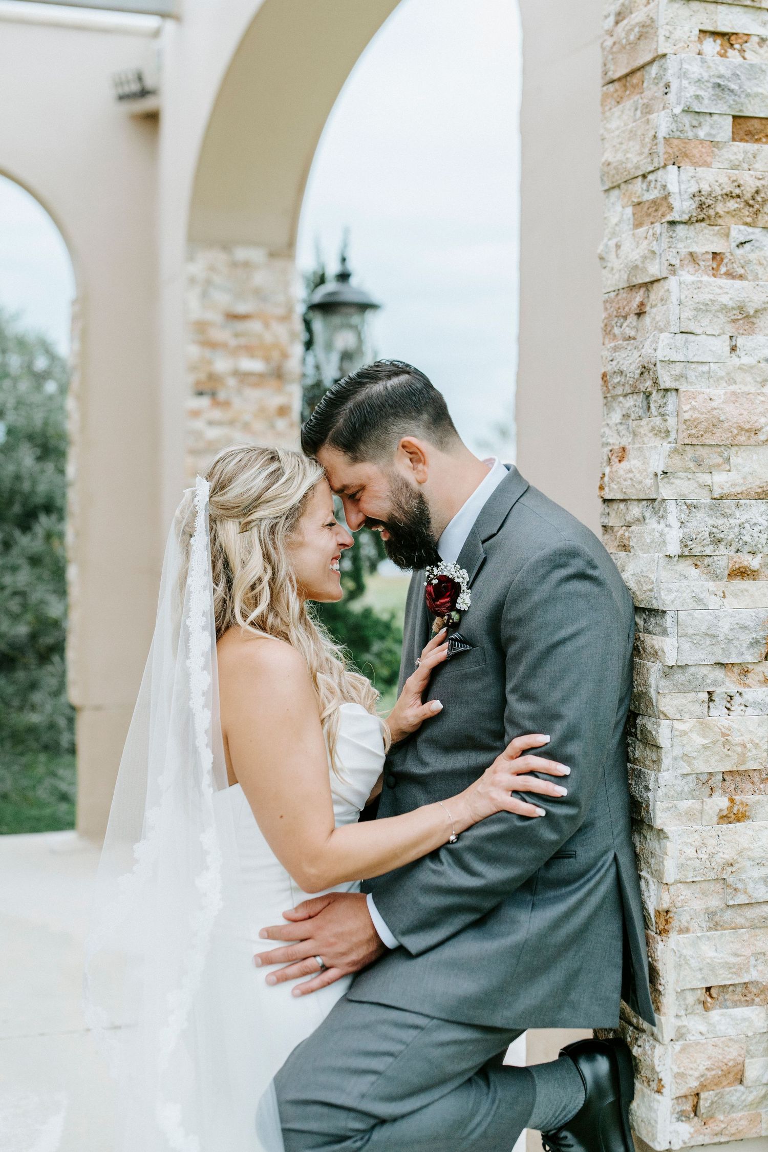 Romantic wedding couple shares intimate moments between elegant stone columns at their venue.