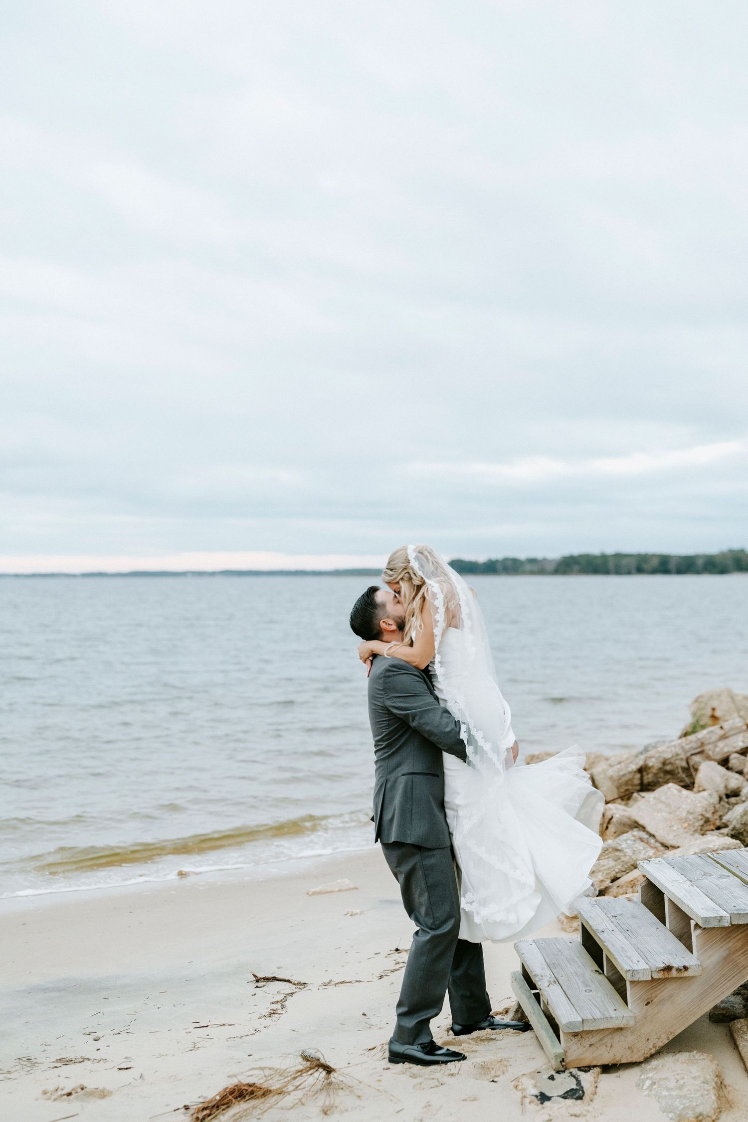 A romantic wedding moment captured on a rocky beach with overcast skies.